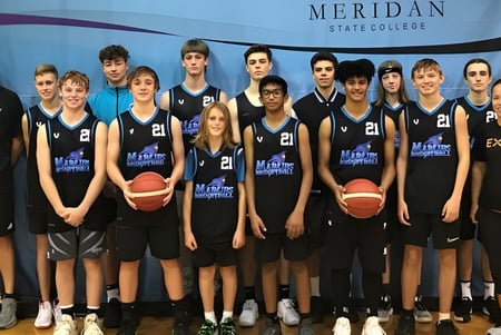 Un grupo de jóvenes jugadores y jugadoras de baloncesto posan frente a un cartel del Meridan State College.