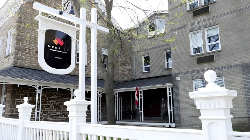 El edificio de piedra con área de entrada blanca de la Merrick Preparatory School está rodeado de árboles.