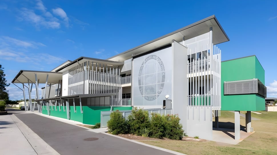 El edificio de varios pisos de la Merrimac State High School con fachadas blancas y verdes y paisaje circundante bajo un cielo azul.