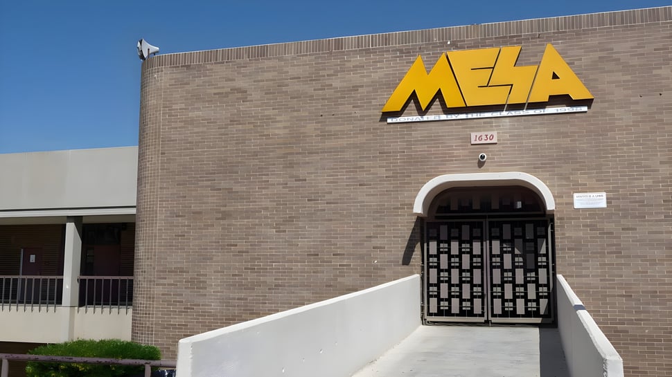 El edificio de ladrillo con un cartel amarillo de MESA muestra la fachada de la Mesa High School bajo un cielo despejado.