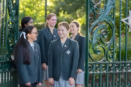 Un grupo de estudiantes está frente a una puerta de metal decorada en el campus del Methodist Ladies' College.