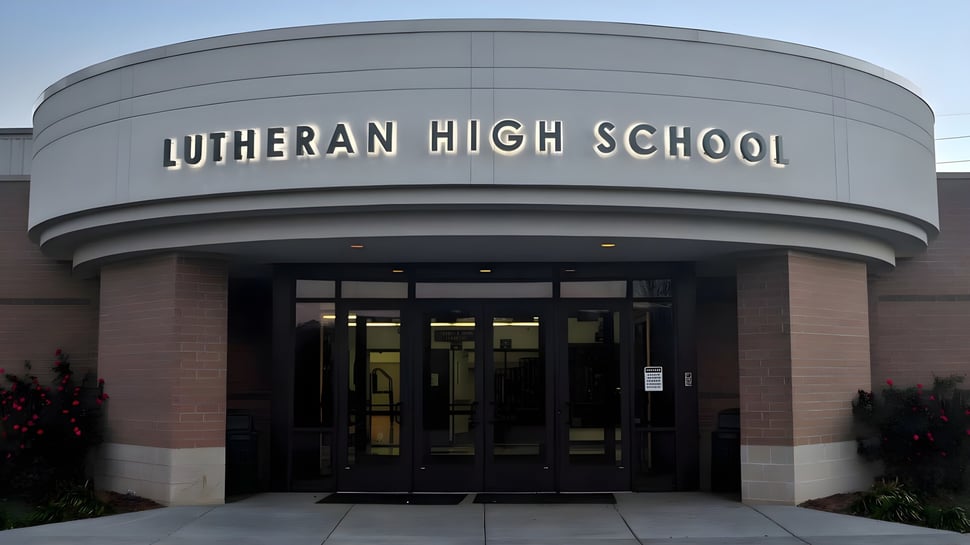 La entrada de la Metro East Lutheran High School muestra un gran edificio moderno con un techo curvado y un llamativo letrero sobre la entrada.