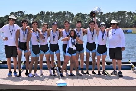 Un grupo de estudiantes de la Miami Beach Senior High School está como equipo de remo juntos en un muelle junto al agua.
