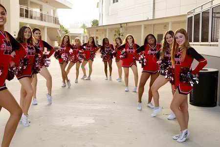 Un grupo de animadoras en uniformes rojos y negros con pompones está en el campus de la Miami-Dade County Public School.