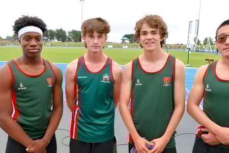 Cuatro jóvenes atletas de la Middleton Grange School están en el campo de deportes frente a las gradas.
