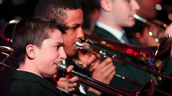 Un niño canta en un concierto en el escenario de la Mill Hill International School con una banda de fondo.