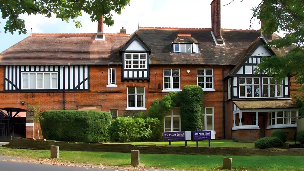 El edificio Tudor de la Mill Hill International School está rodeado de vegetación verde y un césped bien cuidado.