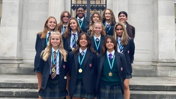 Un grupo de estudiantes está en la escalera frente al edificio representativo de la Mill Hill School y lleva medallas.