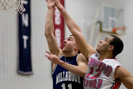 Dos estudiantes de la Millbrook School luchan por el balón en una canasta de baloncesto en el gimnasio.