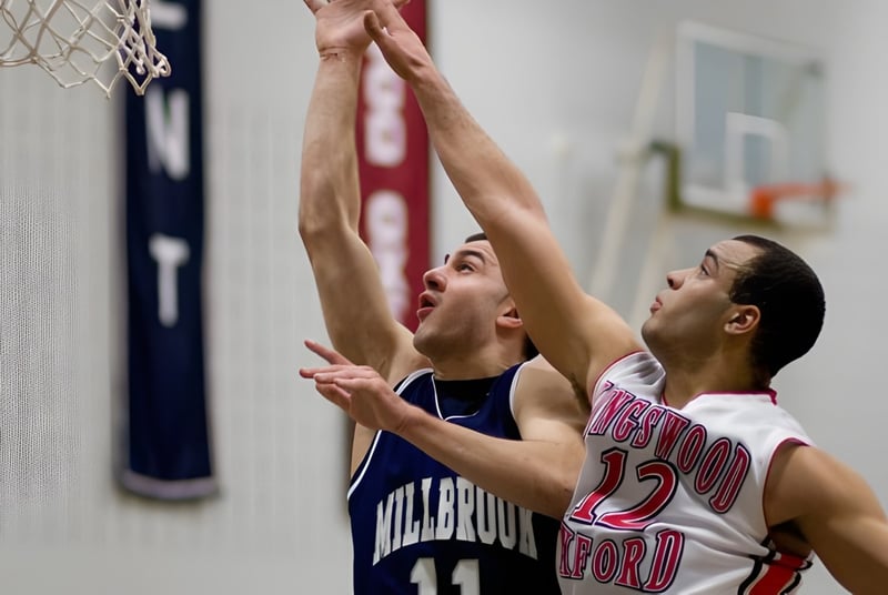 Dos estudiantes de la Millbrook School luchan por el balón en una canasta de baloncesto en el gimnasio.