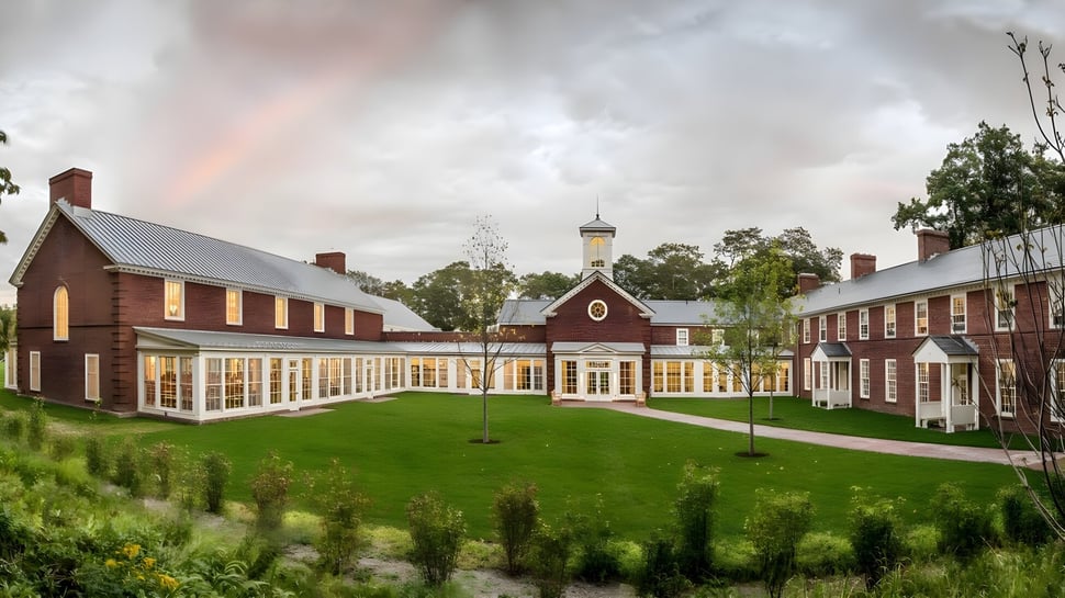 El edificio principal de la Millbrook School con torre central se encuentra frente a un fondo verde y un arcoíris en el cielo nublado.