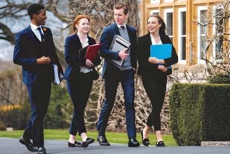 Un grupo de cuatro personas camina por un camino bordeado de árboles en el campus de la Millfield School.