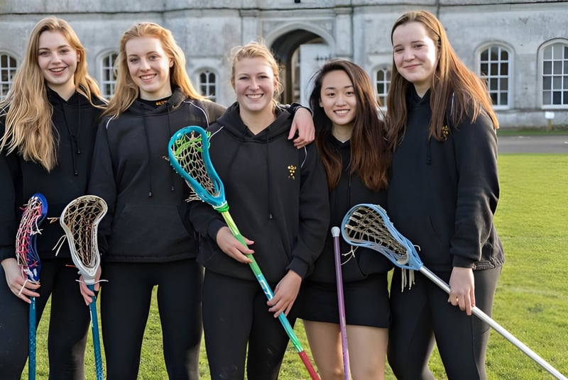 Un grupo de alumnas de la Milton Abbey School está con palos de lacrosse frente a un edificio histórico con ventanas de arco.