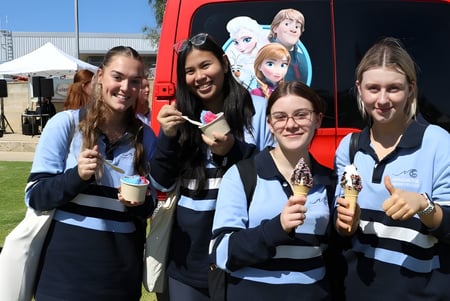 Un grupo de alumnas del Mindarie Senior College posan frente a un vehículo rojo con motivo de Disney en un evento al aire libre.