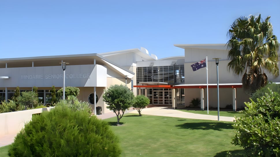 El moderno edificio blanco con palmeras y césped bien cuidado en el campus del Mindarie Senior College bajo un cielo azul claro.