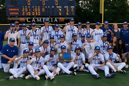 Un grupo de jugadoras y jugadores de béisbol posan en el campo de béisbol de Minnetonka Public Schools frente al marcador.