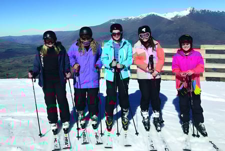 Un grupo de estudiantes de la Miramichi Valley High School está de pie con colorida ropa de invierno en una ladera cubierta de nieve con una cima nevada de fondo.