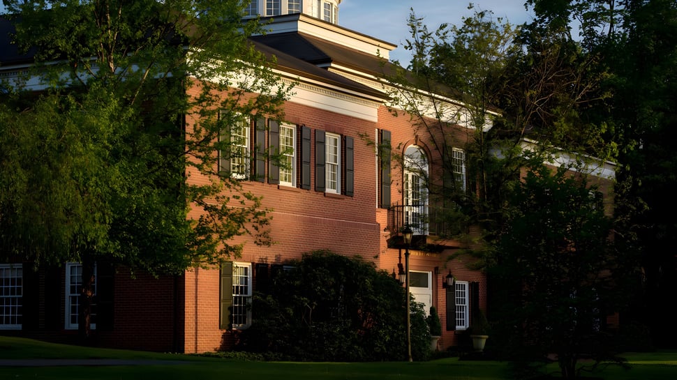 El edificio de ladrillo con arquitectura histórica en el campus de Miss Porter's School está rodeado de vegetación verde.