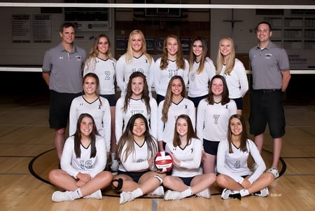 Un grupo de jugadoras de voleibol de la Mission Secondary School posan en la cancha de baloncesto frente al marcador.