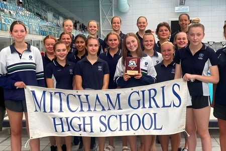 Un grupo de alumnas de la Mitcham Girls High School sostiene un banner en un gimnasio.