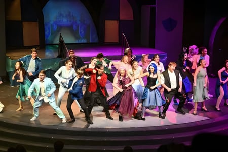 Un grupo de estudiantes en coloridos trajes está en el escenario de la M.M. Robinson High School frente a un fondo abstracto.