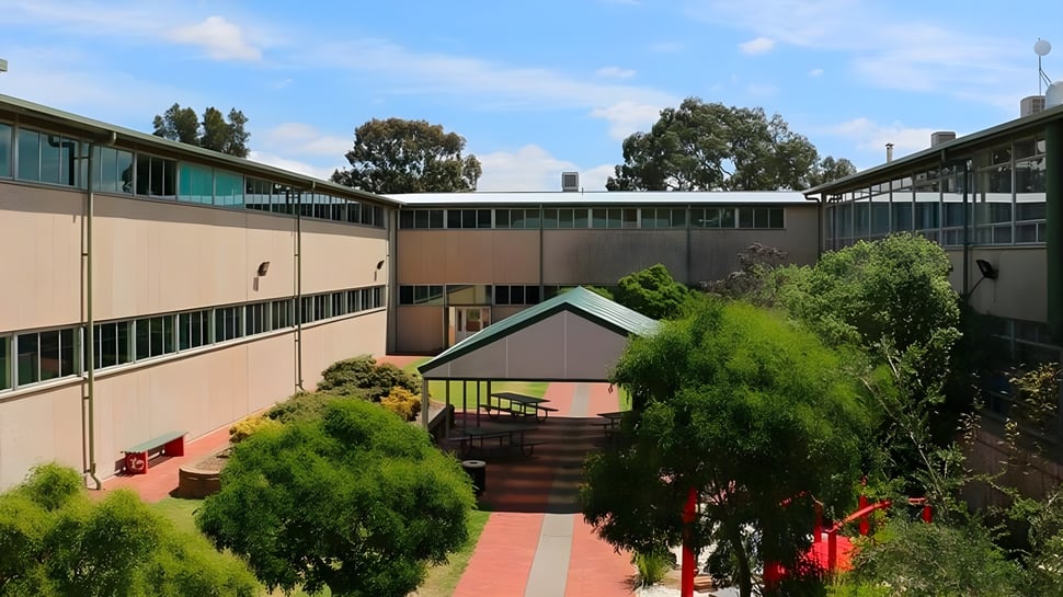 El edificio de varios pisos con patio de Modbury High School está rodeado de árboles y arbustos.