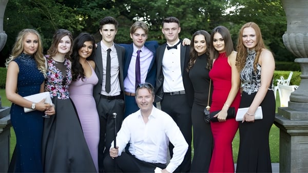 Un grupo de personas bien vestidas está junto a un fondo verde en el terreno de la Monkton Combe School.