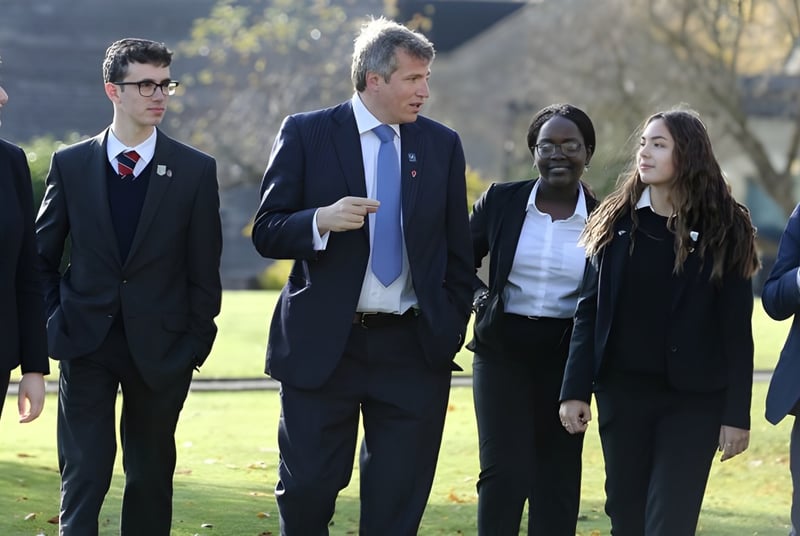 Un grupo de estudiantes de la Monkton Combe School pasea juntos en un campo con árboles de fondo.