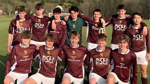 Un grupo de estudiantes de la Monmouth School for Boys posan en un campo deportivo con césped y rodeados de árboles.