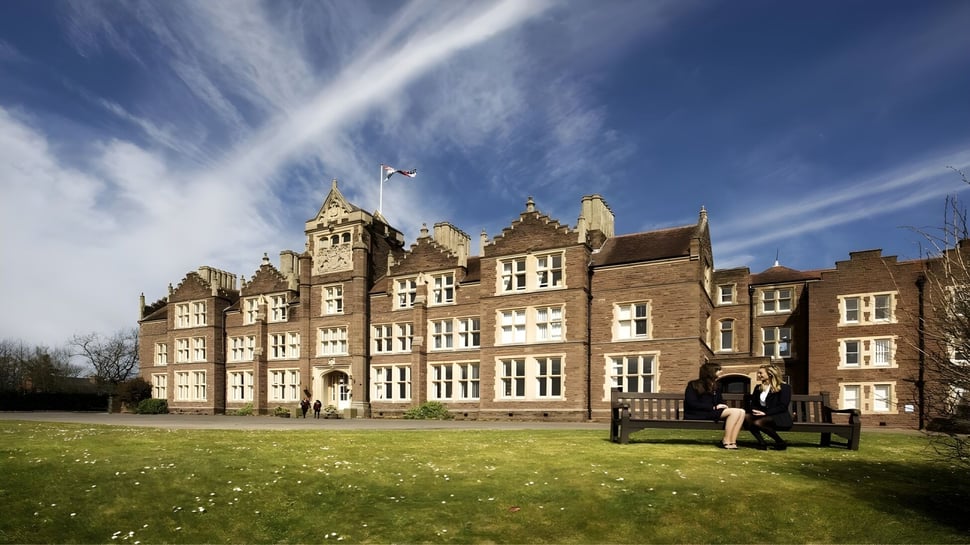 El histórico edificio de la Monmouth School for Girls se encuentra en un campo verde bajo un cielo azul con nubes.