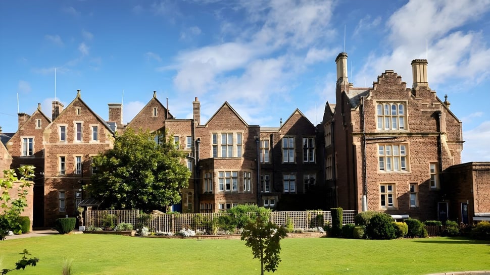 El edificio histórico de la Monmouth School for Boys está rodeado de césped cuidado y vegetación verde.