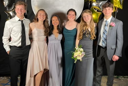 Un grupo de seis personas en ropa formal posando frente a un fondo con globos metálicos en el campus de la Monsignor Donovan Catholic High School.