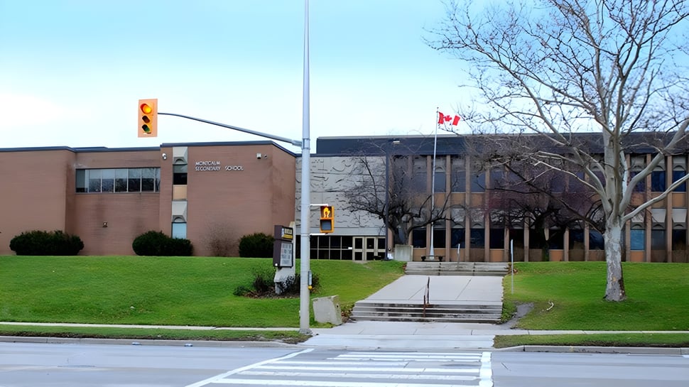 El edificio de ladrillo de la Montcalm Secondary School con una bandera canadiense al frente y árboles al fondo.