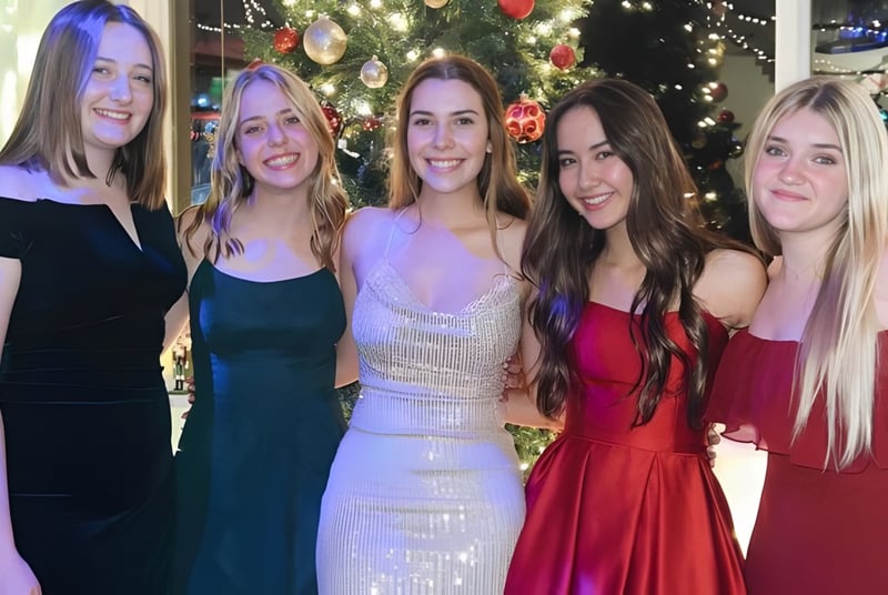 Cinco estudiantes de la Monterey Bay Academy posan juntas frente a un árbol de Navidad decorado festivamente.