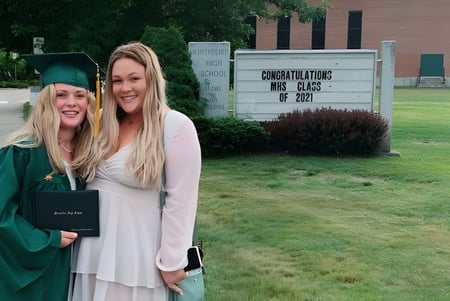 Dos estudiantes en togas de graduación están frente a un cartel con felicitaciones a la clase de 2022 en el campus de la Montpelier High School.