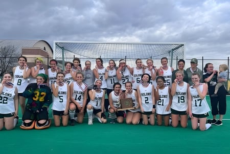 Un grupo de jóvenes deportistas posando en el campo de hockey de la Montpelier Roxbury Public School District bajo un cielo nublado.