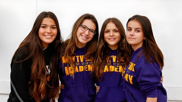 Cuatro alumnas de la Montverde Academy posan riendo frente a una pared blanca en sudaderas moradas uniformes.
