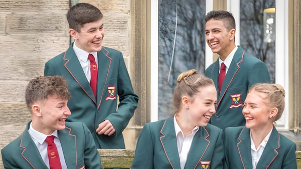 Un grupo de estudiantes en uniformes escolares está frente a un edificio de ladrillo en el terreno de la Moorland School y están conversando.