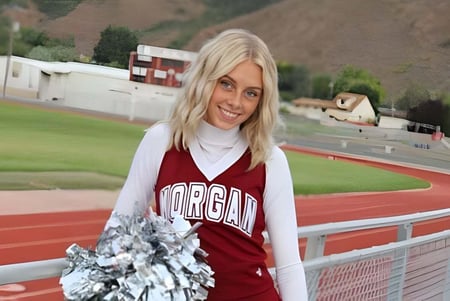 Una joven en camiseta roja sonríe en la pista de la Morgan High School con césped y edificios al fondo.