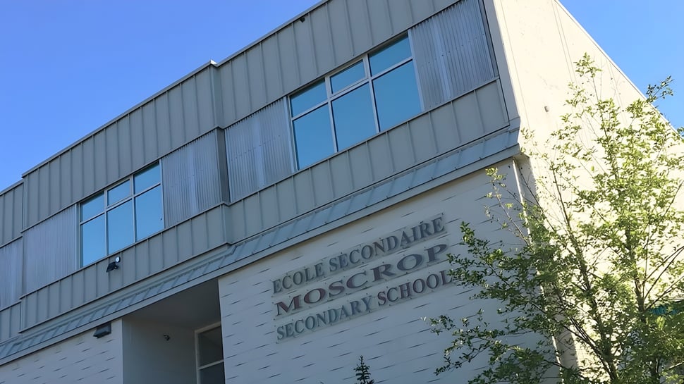El moderno edificio escolar de la Moscrop School con grandes ventanas y un letrero claramente legible está rodeado de árboles.