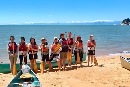 Un grupo de estudiantes de la Motueka High School está en la playa con una isla rocosa al fondo.