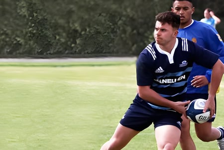 Un estudiante de Mount Albert Grammar sostiene un balón de rugby en un campo cubierto de hierba.