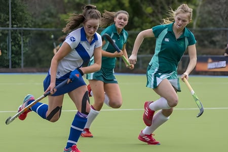Estudiantes de la Mount Anville Secondary School juegan un partido de hockey en un campo deportivo con valla.