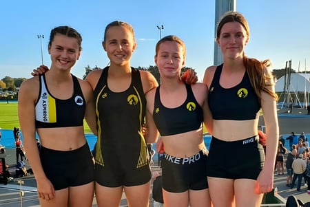 Cuatro alumnas del Mount Aspiring College posan juntas en un campo deportivo frente a un estadio.