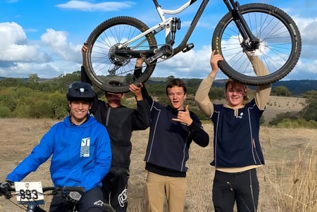 Estudiantes de la Mount Barker High School sostienen una bicicleta de montaña en un campo ondulado con cielo nublado.