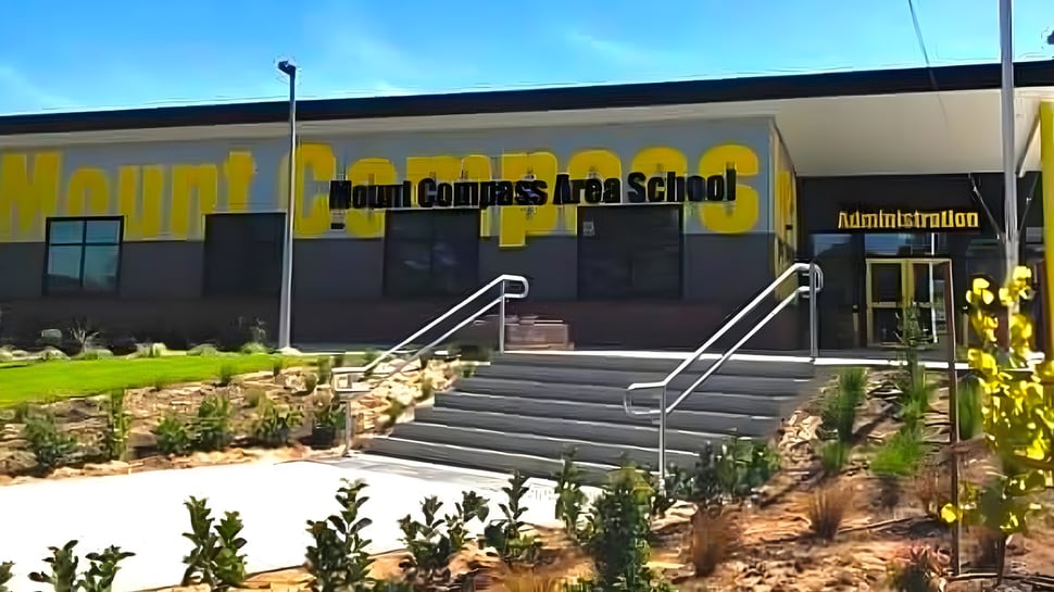 Se puede ver el edificio de la Mount Compass Area School con un gran letrero amarillo y una escalera hacia la entrada.