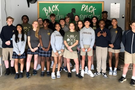 Un grupo de estudiantes de la Mount De Sales Academy está frente a un cartel con la inscripción Back Pack.