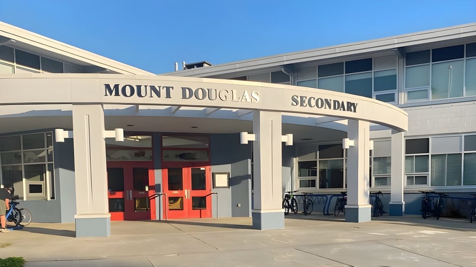 El moderno edificio escolar de la Mount Douglas Secondary School con puertas de entrada rojas y un cielo azul de fondo.