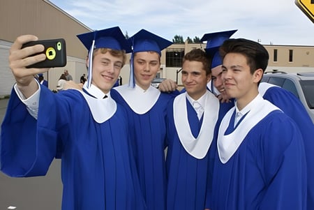 Un grupo de jóvenes en togas de graduación azules se toma un selfie en el campus de la Mount Elizabeth Middle/Secondary School.