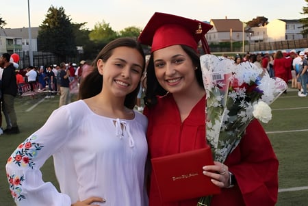 Dos estudiantes de la Mount Everett Regional High School posan con vestimenta de graduación frente a una multitud en un campo deportivo.